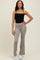 woman wearing a black spaghetti strap top and beige flared workout pants, standing with one hand on her hip