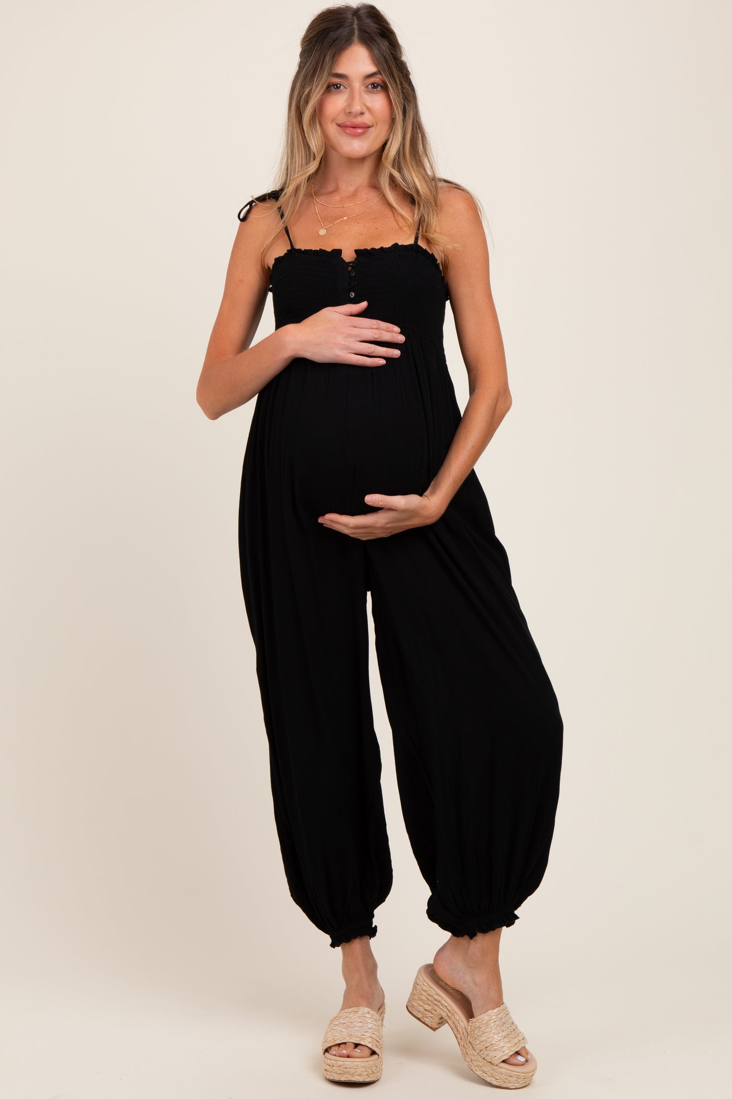 woman wearing a black maternity jumpsuit with a smocked bodice and baggy pants, holding her baby bump
