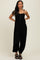woman wearing a black smocked jumpsuit with adjustable straps and button detail, standing confidently with hands on hips