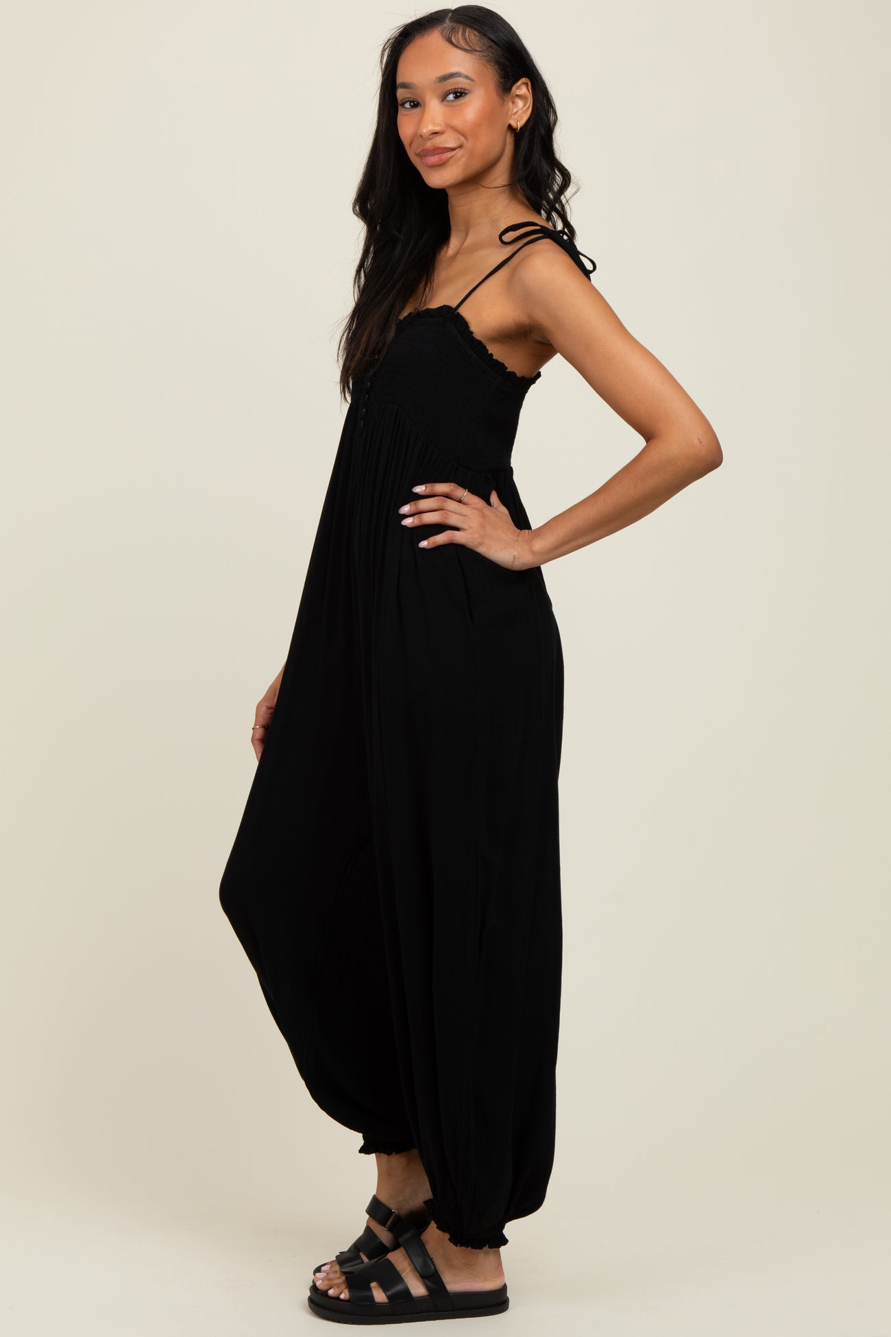 woman wearing a black loose-fitting maxi jumpsuit with a smocked bodice and adjustable straps