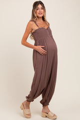 woman wearing a brown maternity jumpsuit with button details and a visible baby bump