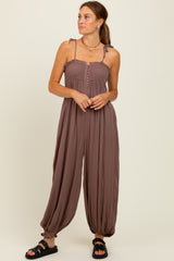 woman wearing a brown sleeveless jumpsuit with button details and flowy pants, standing against a light background