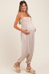 woman wearing a beige maternity jumpsuit with a smocked bodice and a visible baby bump