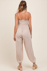 woman wearing a beige maternity jumpsuit with adjustable straps and loose-fitting legs, viewed from the back