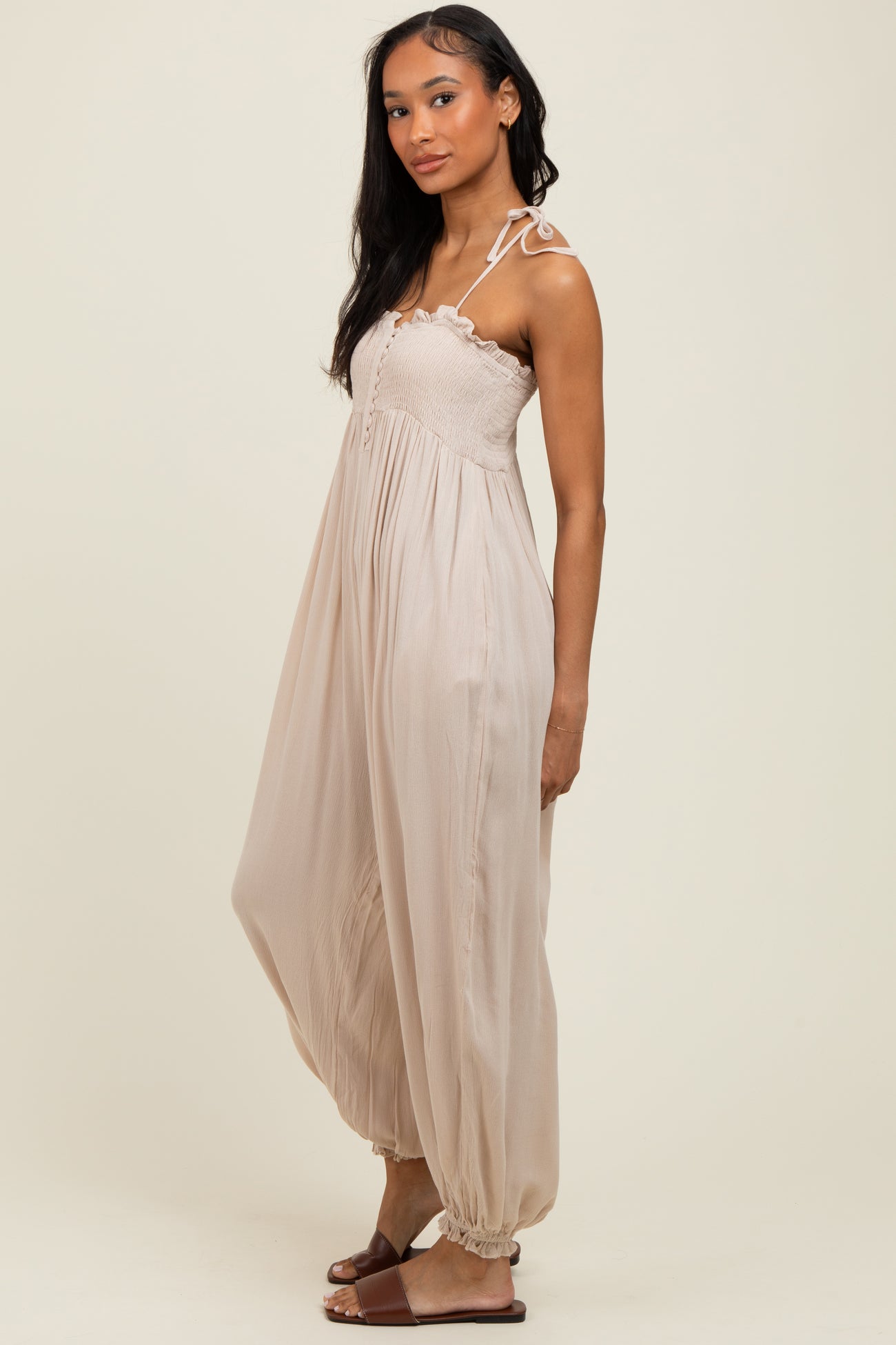 woman wearing a beige sleeveless maxi dress with a smocked bodice and tie straps, standing sideways
