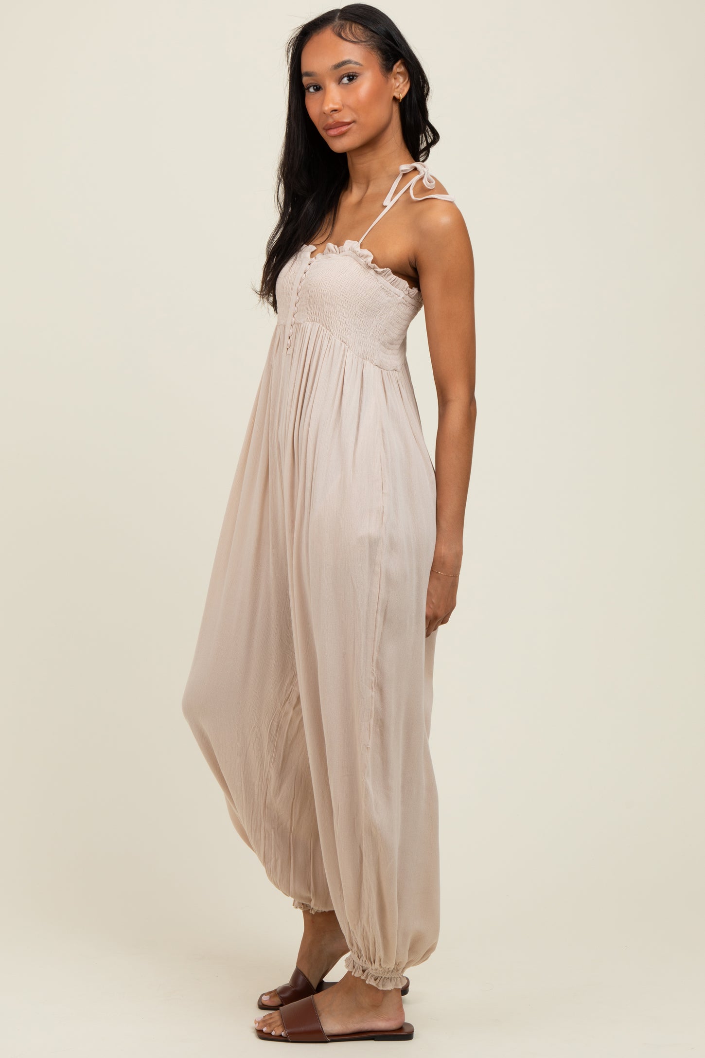 woman wearing a beige sleeveless maxi dress with a smocked bodice and tie straps, standing sideways