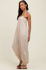 woman wearing a beige sleeveless maxi dress with a smocked bodice and tie straps, standing sideways