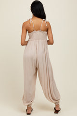 woman wearing a beige sleeveless jumpsuit with adjustable shoulder straps and a smocked bodice, viewed from the back