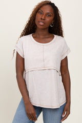 woman wearing a light beige short sleeve top with a layered design and relaxed fit, paired with blue jeans