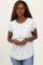 woman wearing a light gray short sleeve top with a layered style and rolled cuffs, standing with a neutral expression
