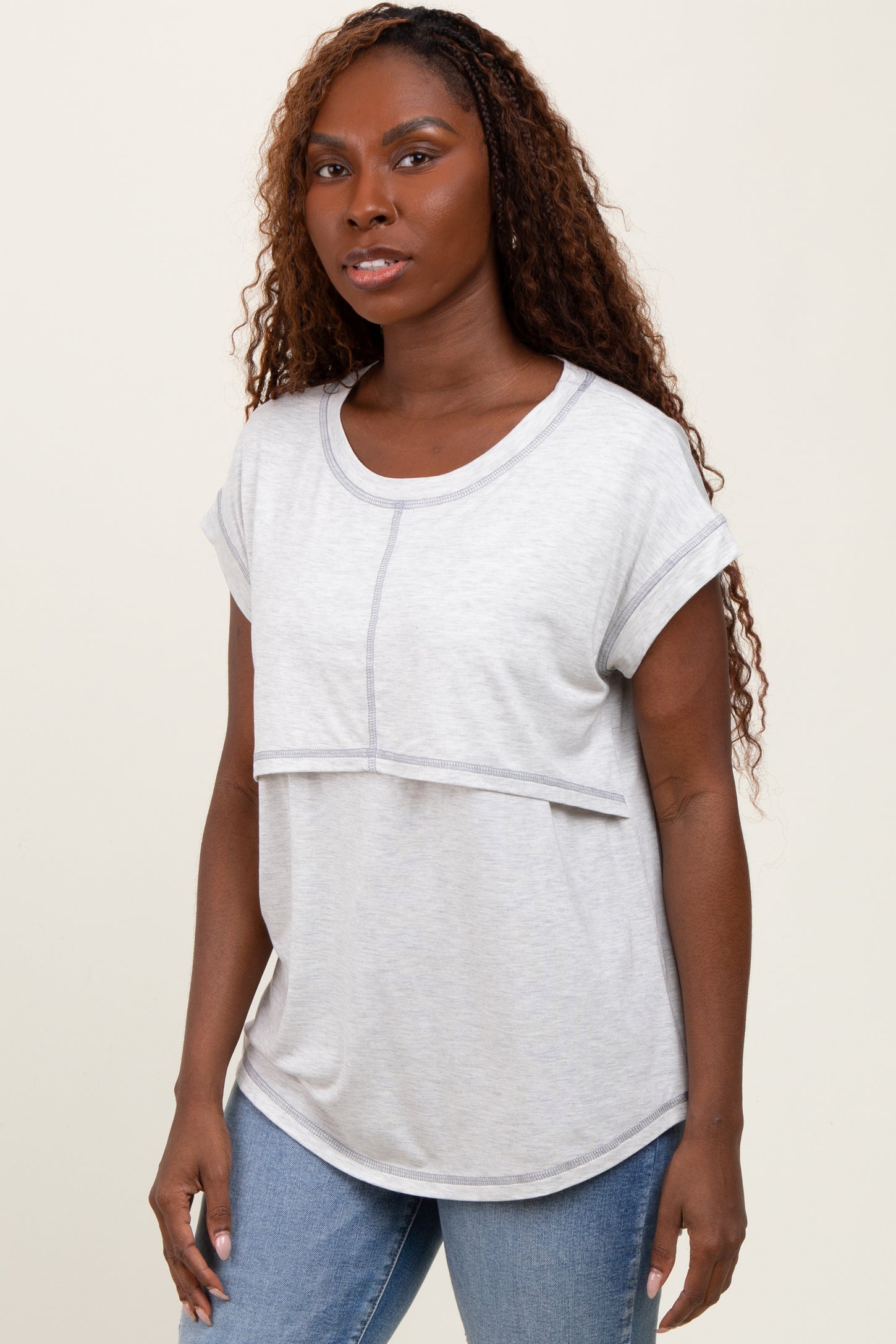 woman wearing a light gray short sleeve top with a layered design and rolled sleeves, styled with blue jeans