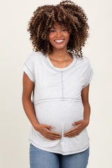 woman wearing a light gray short sleeve maternity top and holding her baby bump