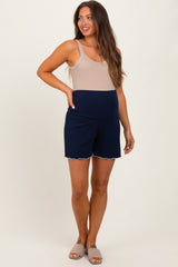 woman wearing a beige maternity tank top and navy maternity shorts with scalloped edges, showcasing her baby bump
