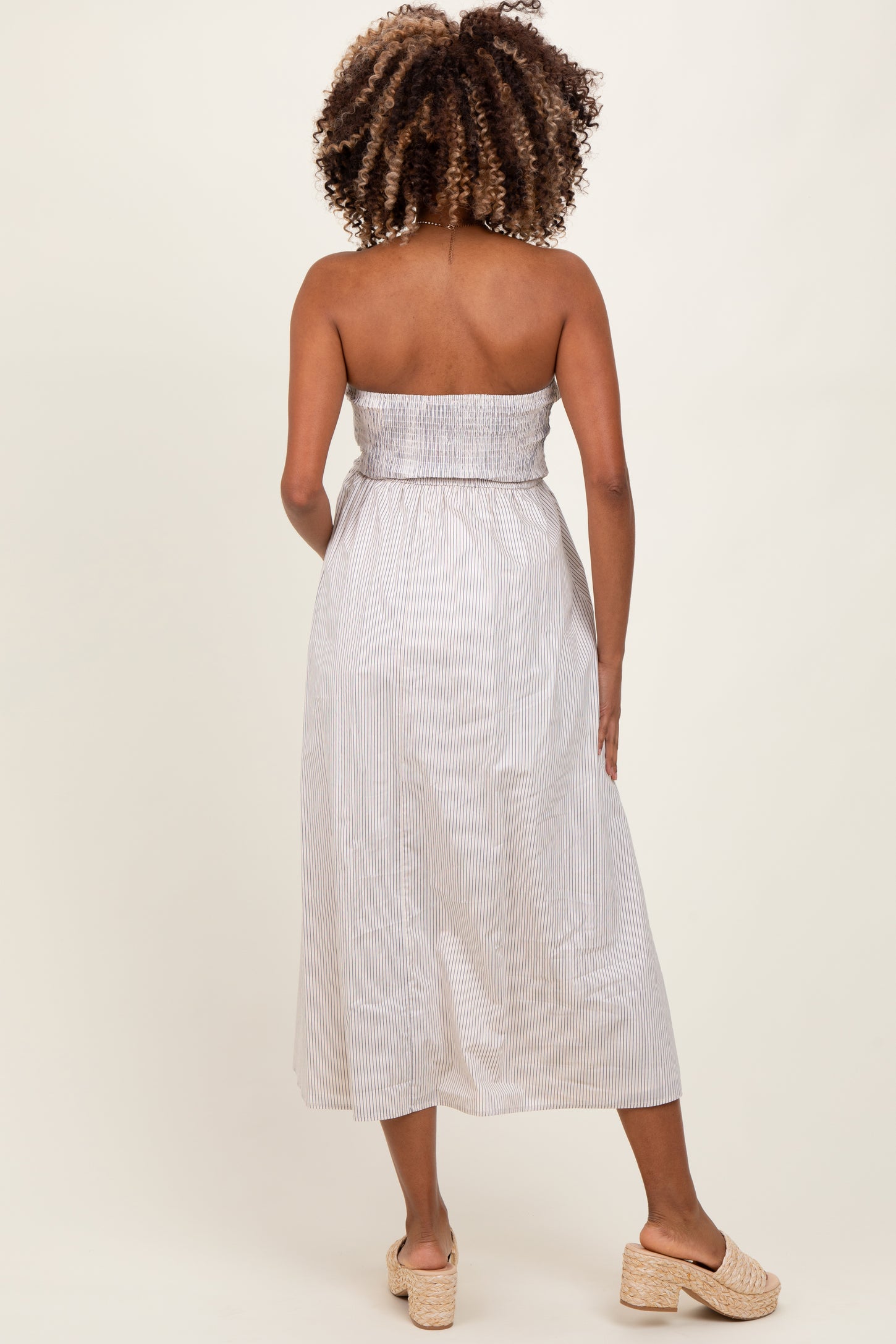 woman wearing a striped strapless maternity dress with a smocked bodice, showing off her baby bump from the back