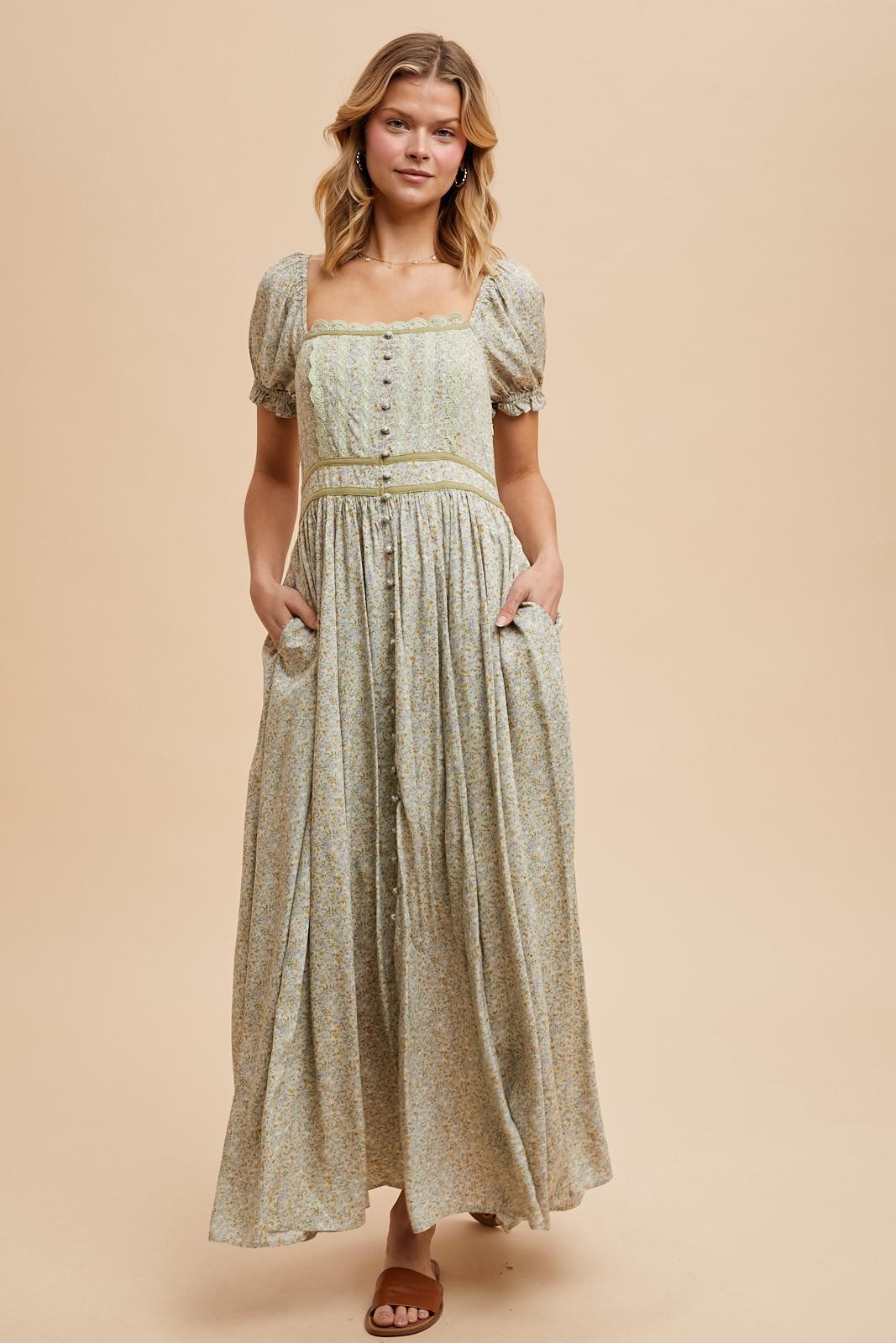 woman wearing a light green floral maxi dress with short puff sleeves and pockets, standing against a neutral background