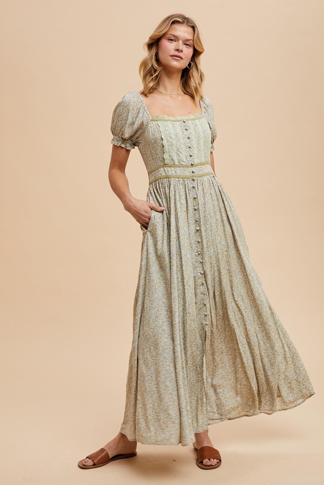 woman wearing a light green floral maxi dress with puff sleeves and a button-down front, standing with hands in pockets