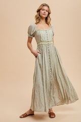 woman wearing a light green floral maxi dress with puff sleeves and a button-down front, standing with hands in pockets