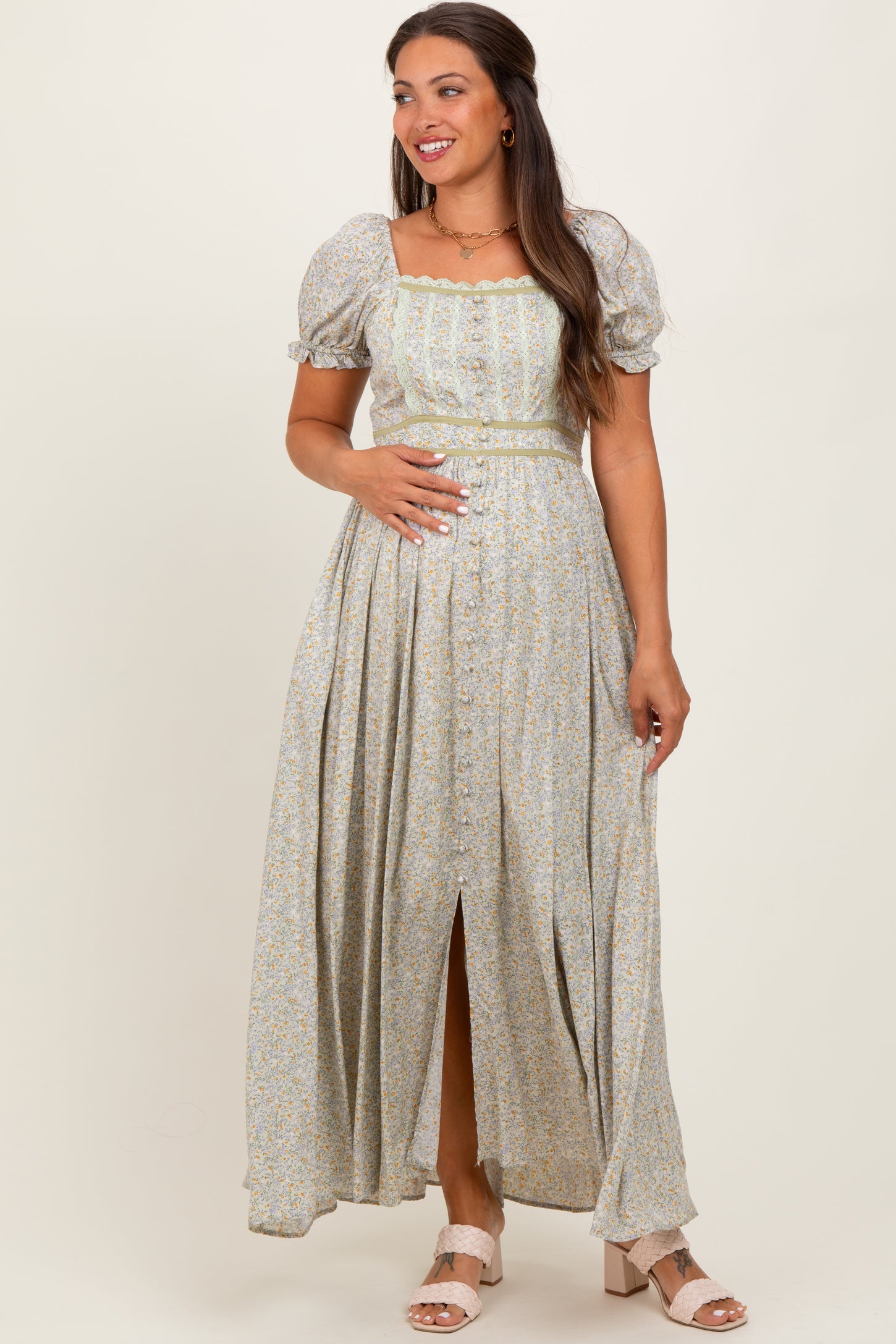 woman wearing a light green floral maternity maxi dress with puff sleeves and a front slit, holding her baby bump