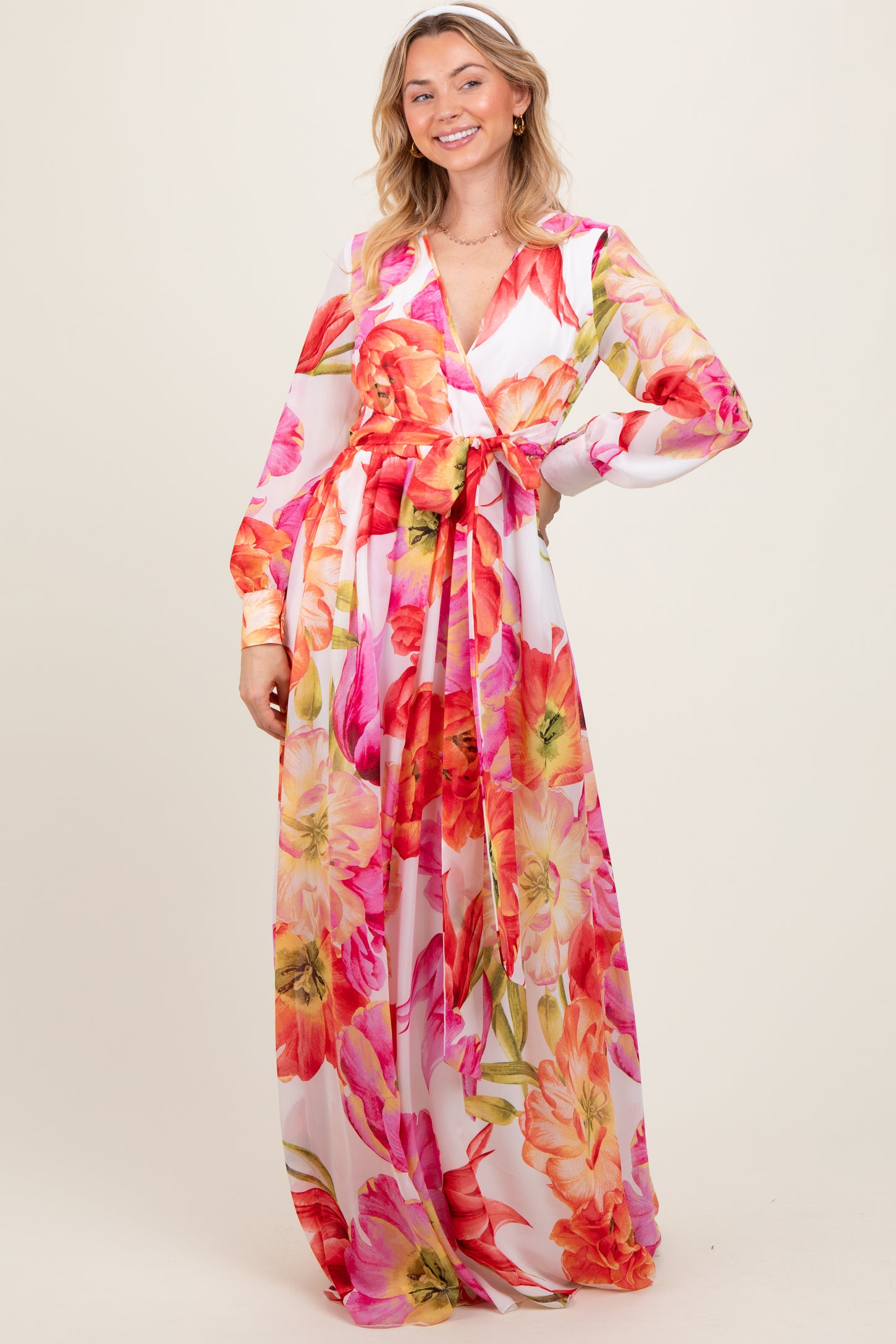 woman wearing a floral long sleeve maxi dress with pink and orange flowers and a tie waist detail