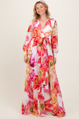 woman wearing a long floral maxi dress with a wrap tie and long sleeves in vibrant pink and orange colors