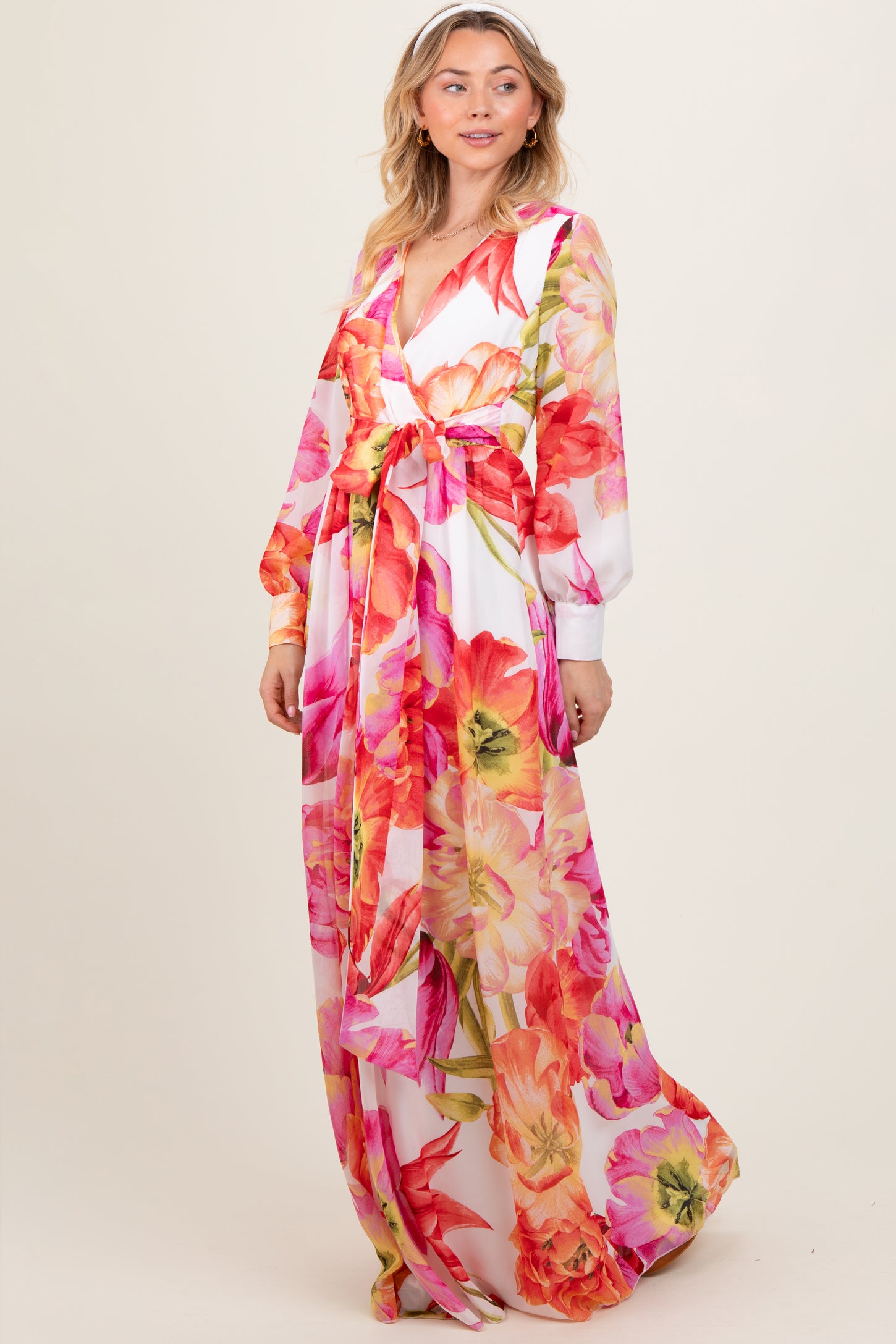 woman wearing a long floral dress with vibrant pink and orange flowers and a tie waist detail