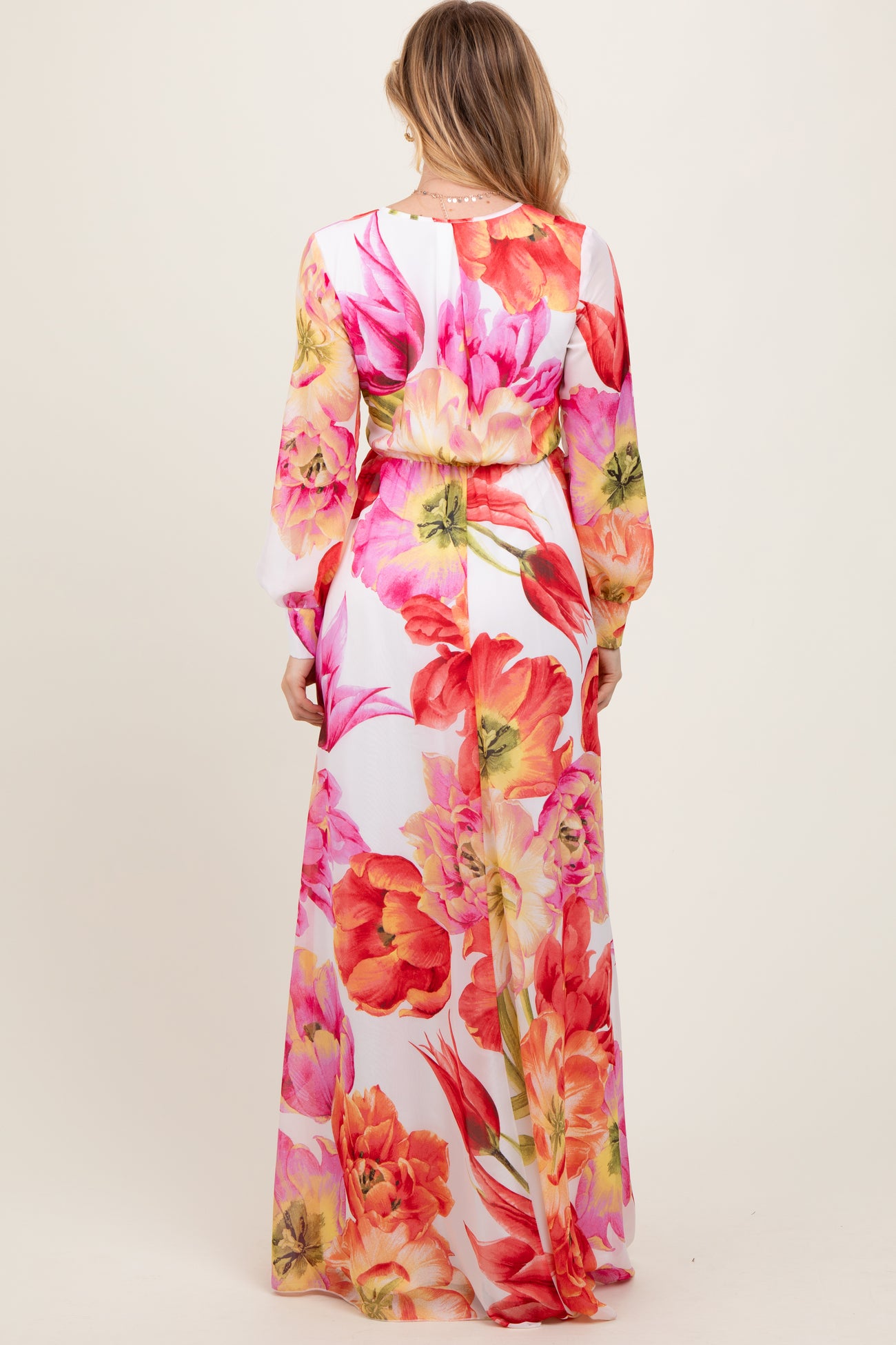 woman wearing a long floral maxi dress with a fitted waist and long sleeves, showing vibrant pink and orange flowers