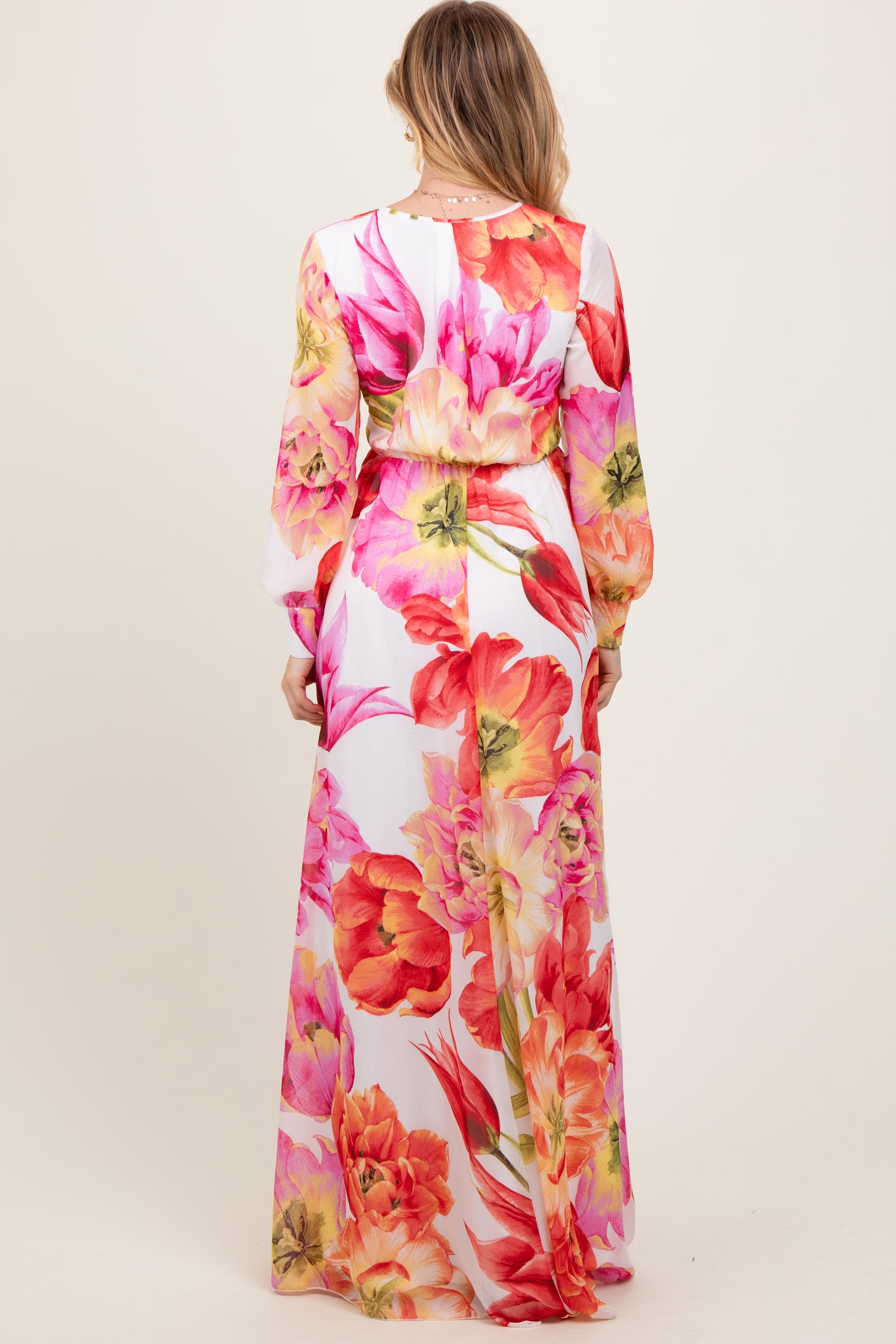 woman wearing a long floral maxi dress with a fitted waist and long sleeves, showing vibrant pink and orange flowers