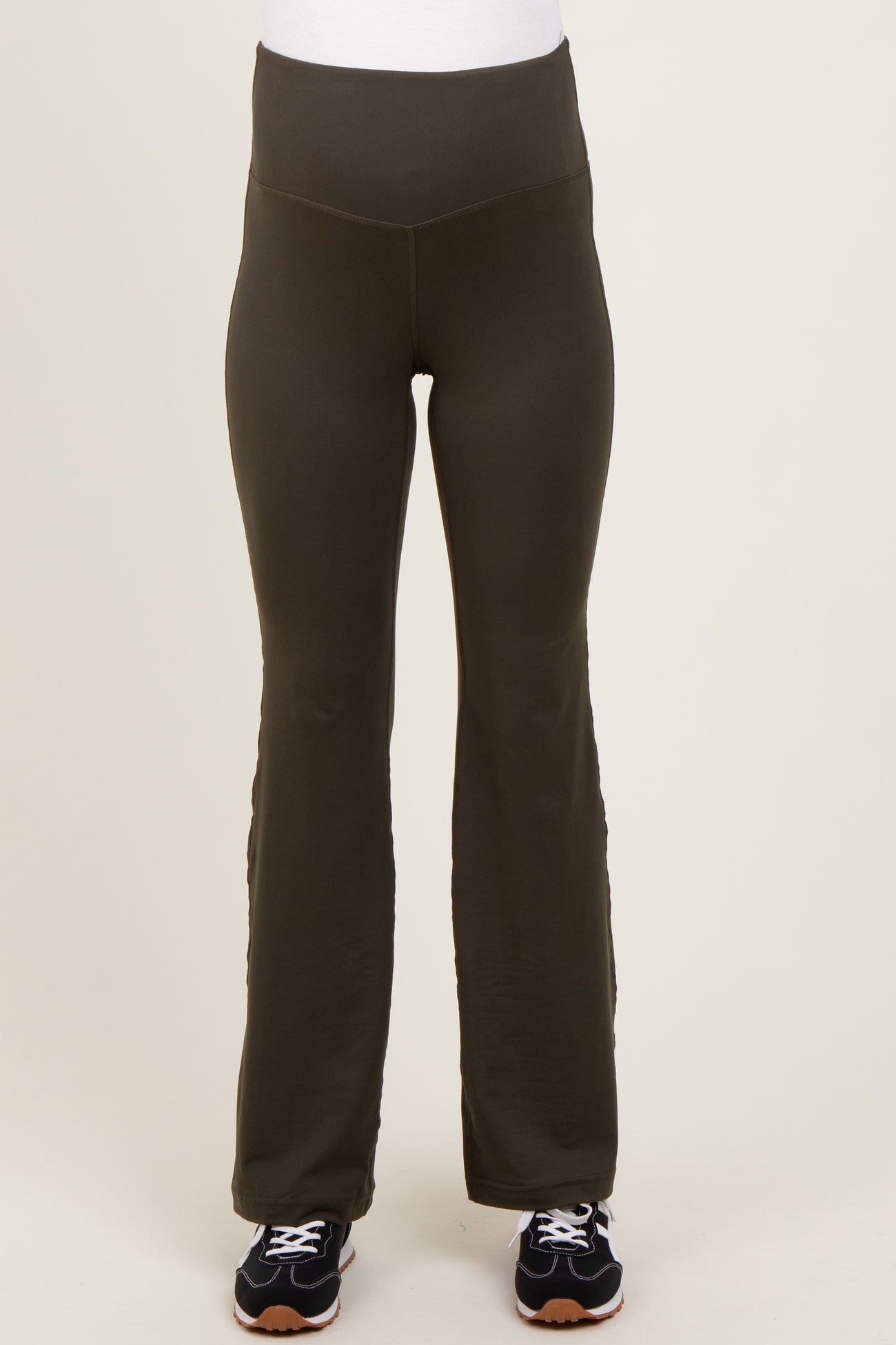 woman wearing dark green maternity active pants with a high waistband and a flared leg, paired with black sneakers