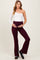 woman wearing a white one shoulder top and burgundy maternity flare pants with a visible baby bump