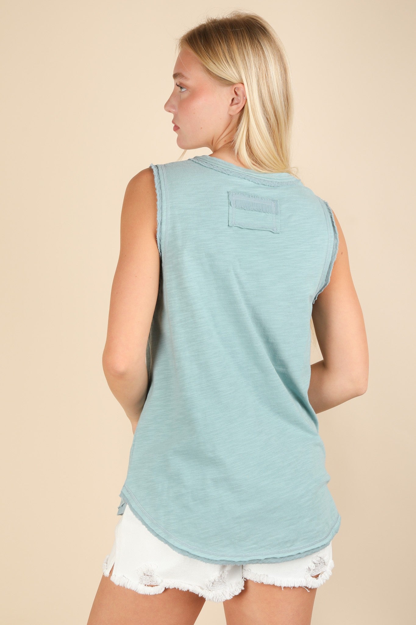 woman wearing a light blue sleeveless top with a rounded hem and patch detail, styled with white distressed shorts