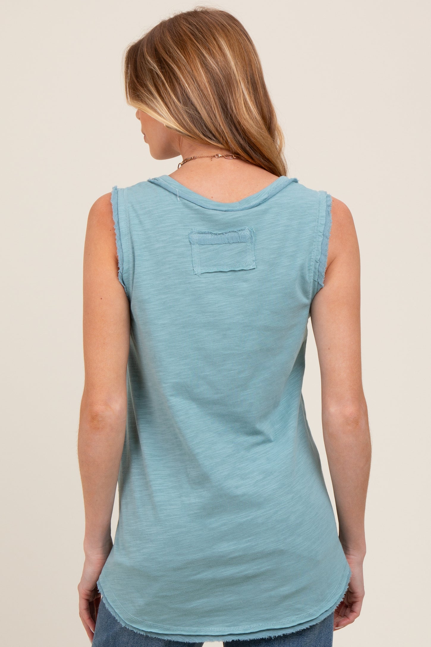 woman wearing a back view of a light blue sleeveless maternity top with a relaxed fit