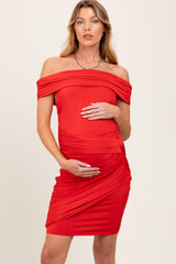 woman wearing a red off-shoulder maternity dress with gathered details and holding her baby bump