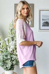 woman wearing a light purple top with decorative short sleeves and paired with distressed denim shorts