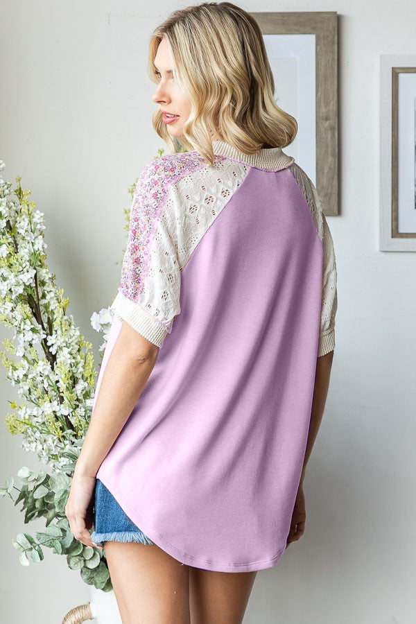 woman wearing a lavender oversized top with lace and floral detail on sleeves, standing with back to camera