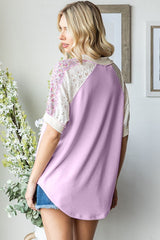 woman wearing a lavender oversized top with lace and floral detail on sleeves, standing with back to camera