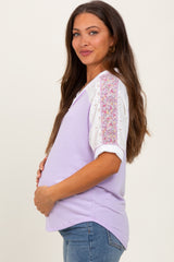 woman wearing a purple maternity top with lace floral sleeves and holding her baby bump