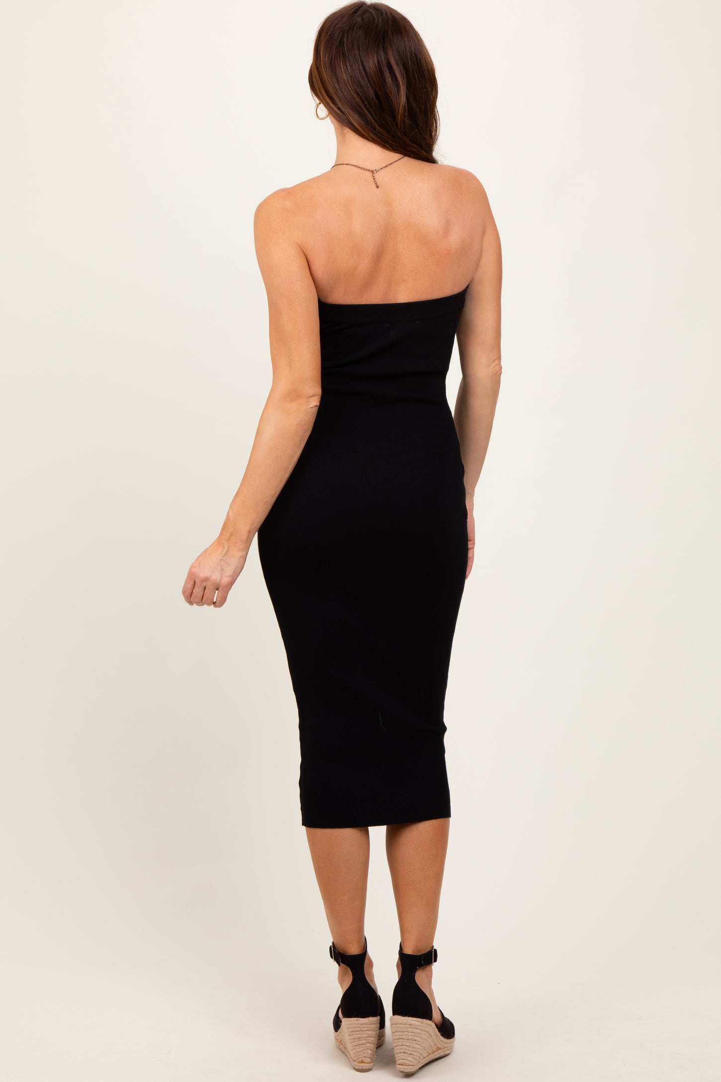 woman wearing a black ribbed midi strapless dress and tan wedge heels, viewed from the back