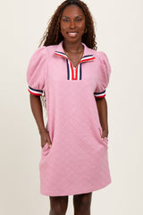 woman wearing a pink short sleeve polo dress with puff sleeves and striped collar details, standing with hands in pockets