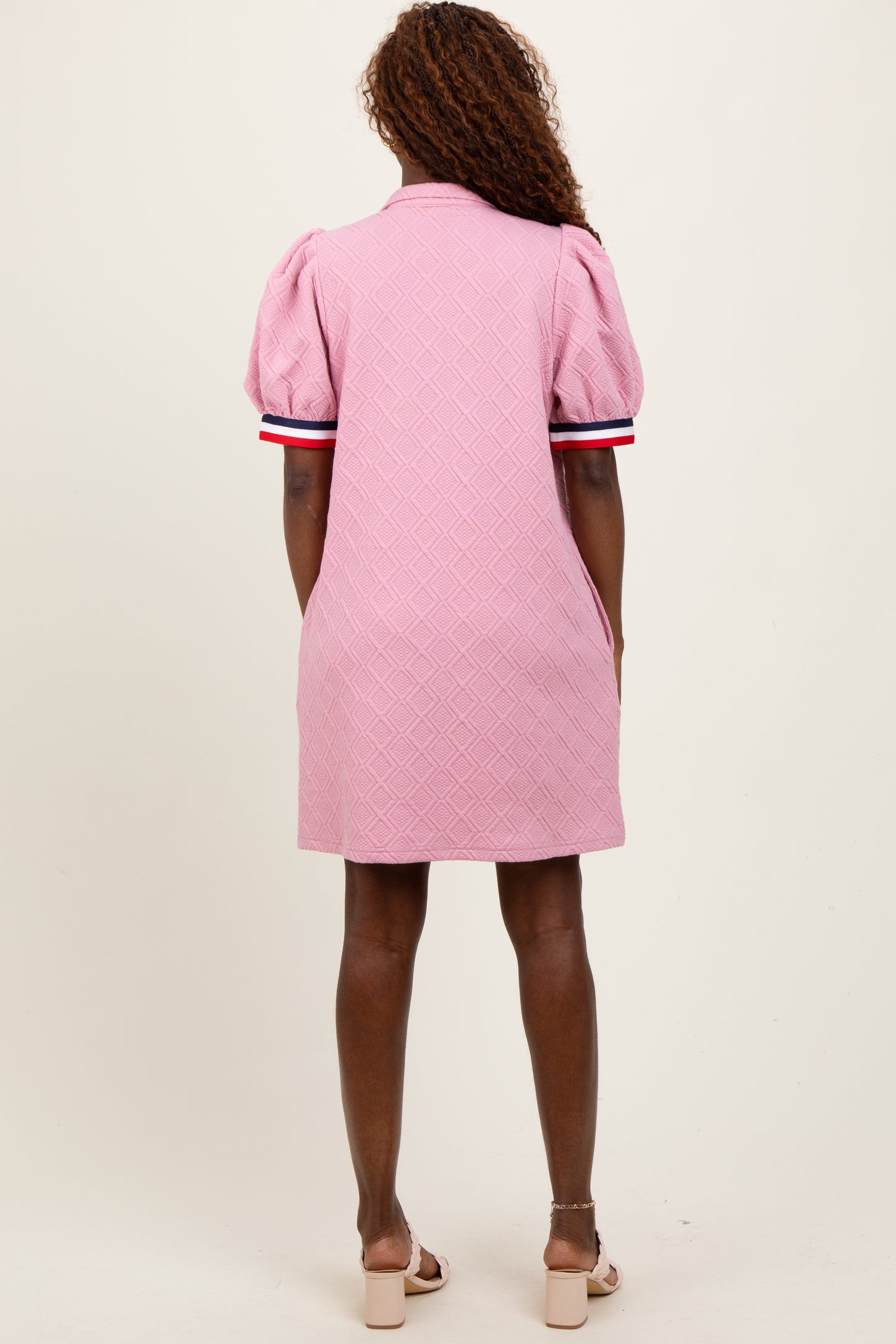 woman wearing a pink short-sleeve puffed dress with a textured pattern and contrast stripes on the sleeves