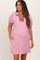 woman wearing a light pink maternity dress with puff sleeves, a zip collar, and red and blue stripes, featuring side pockets