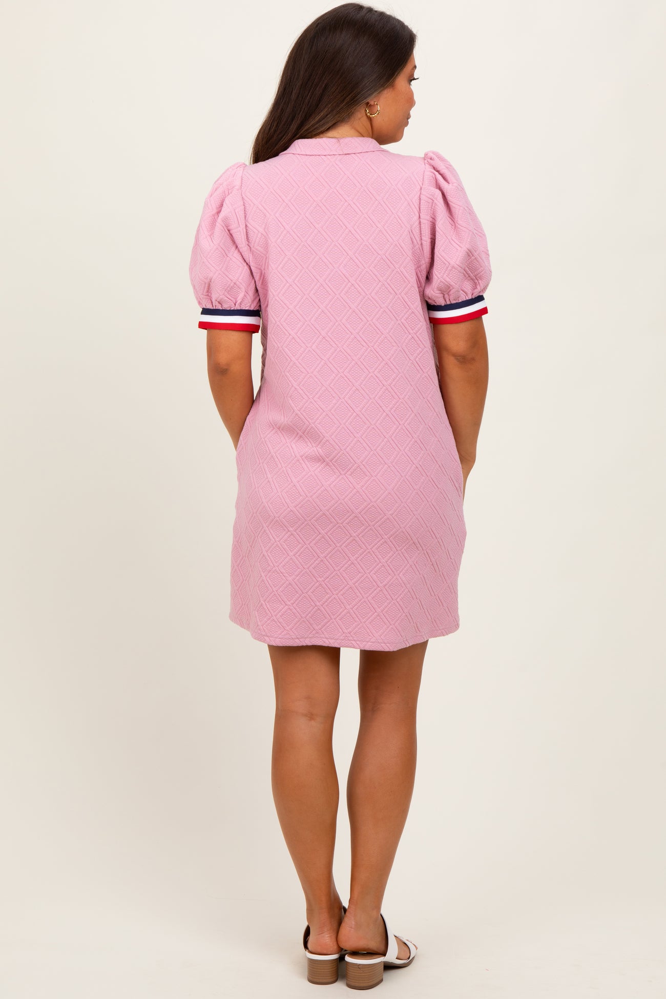 woman wearing a pink maternity dress with puff sleeves and striped details on the sleeves, showing her back