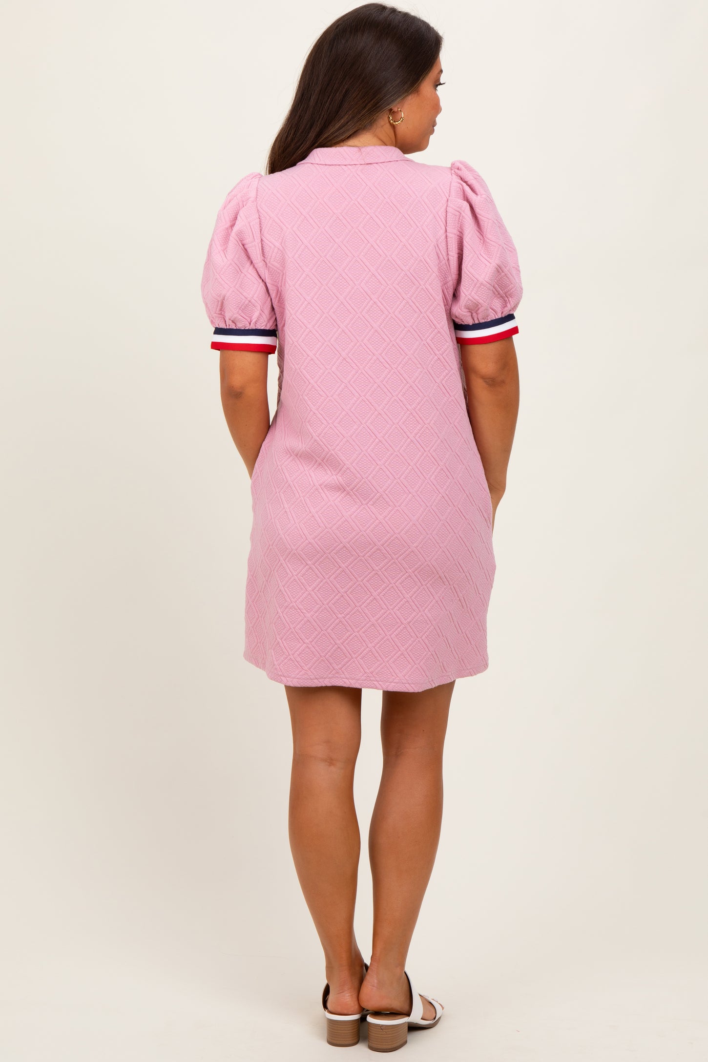 woman wearing a pink maternity dress with puff sleeves and striped details on the sleeves, showing her back