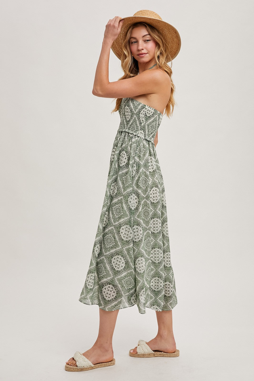 woman wearing a green strapless maxi dress with a patterned design and a straw hat, standing sideways