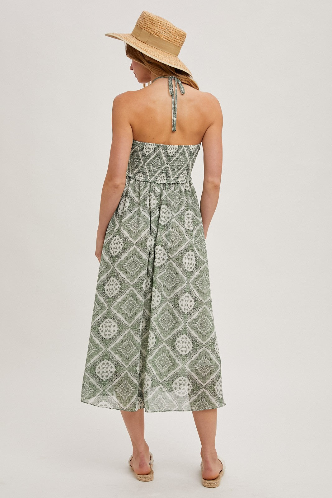 woman wearing a green patterned midi dress with a halter neckline and a straw hat, seen from the back