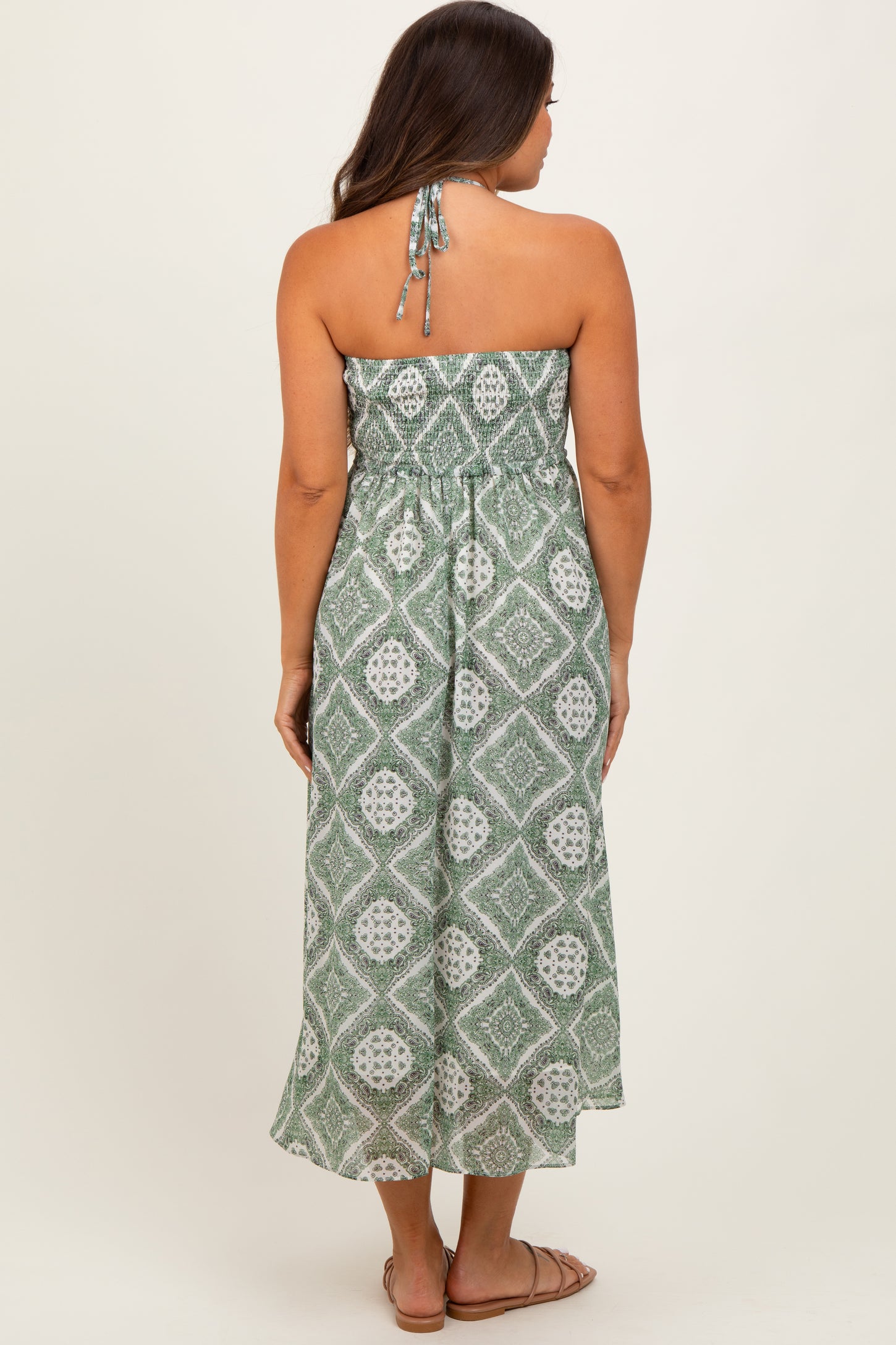 woman wearing a green patterned strapless maternity maxi dress, showing a baby bump from the back