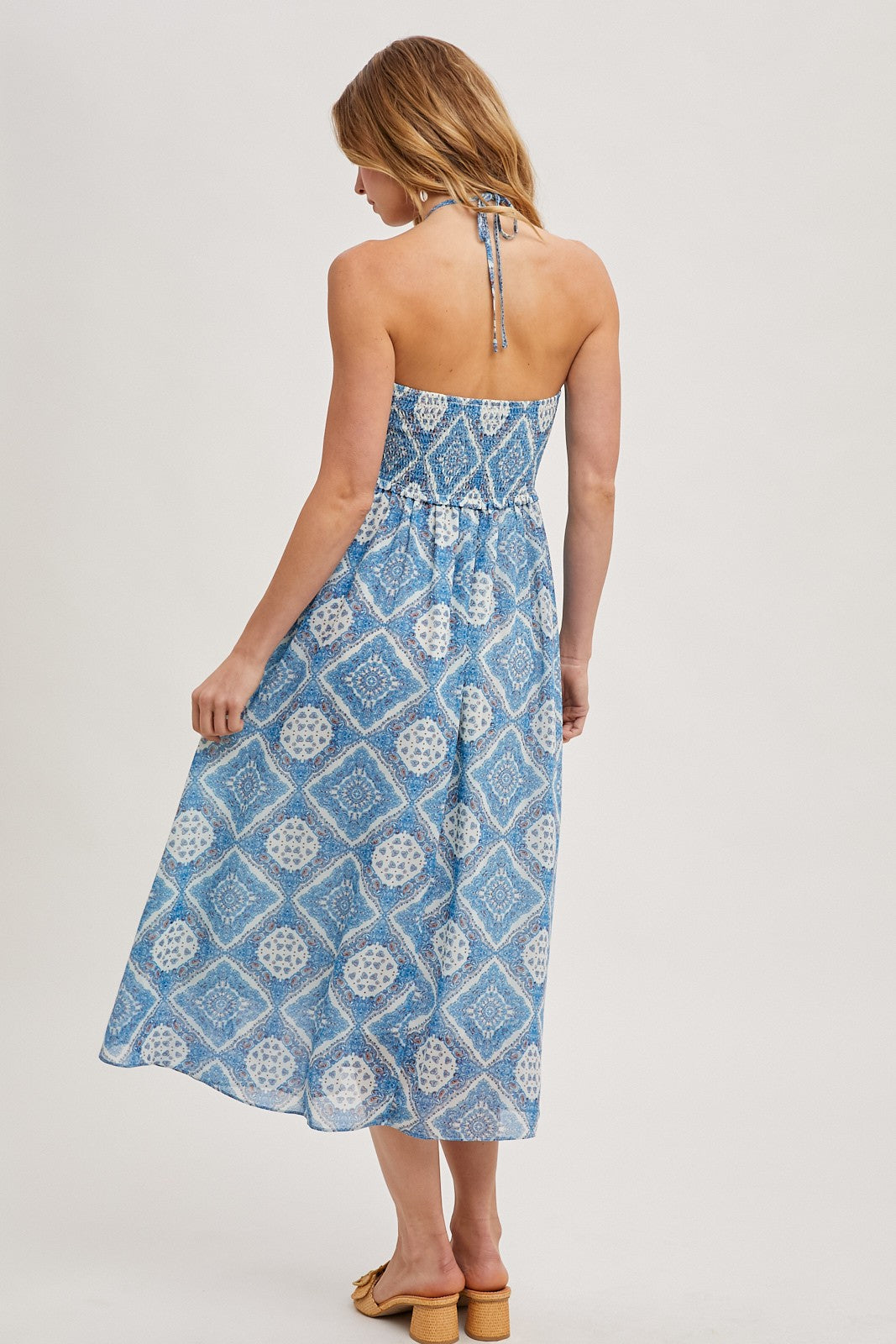 woman wearing a blue patterned maxi dress with a halter neckline and open back, shown from the back