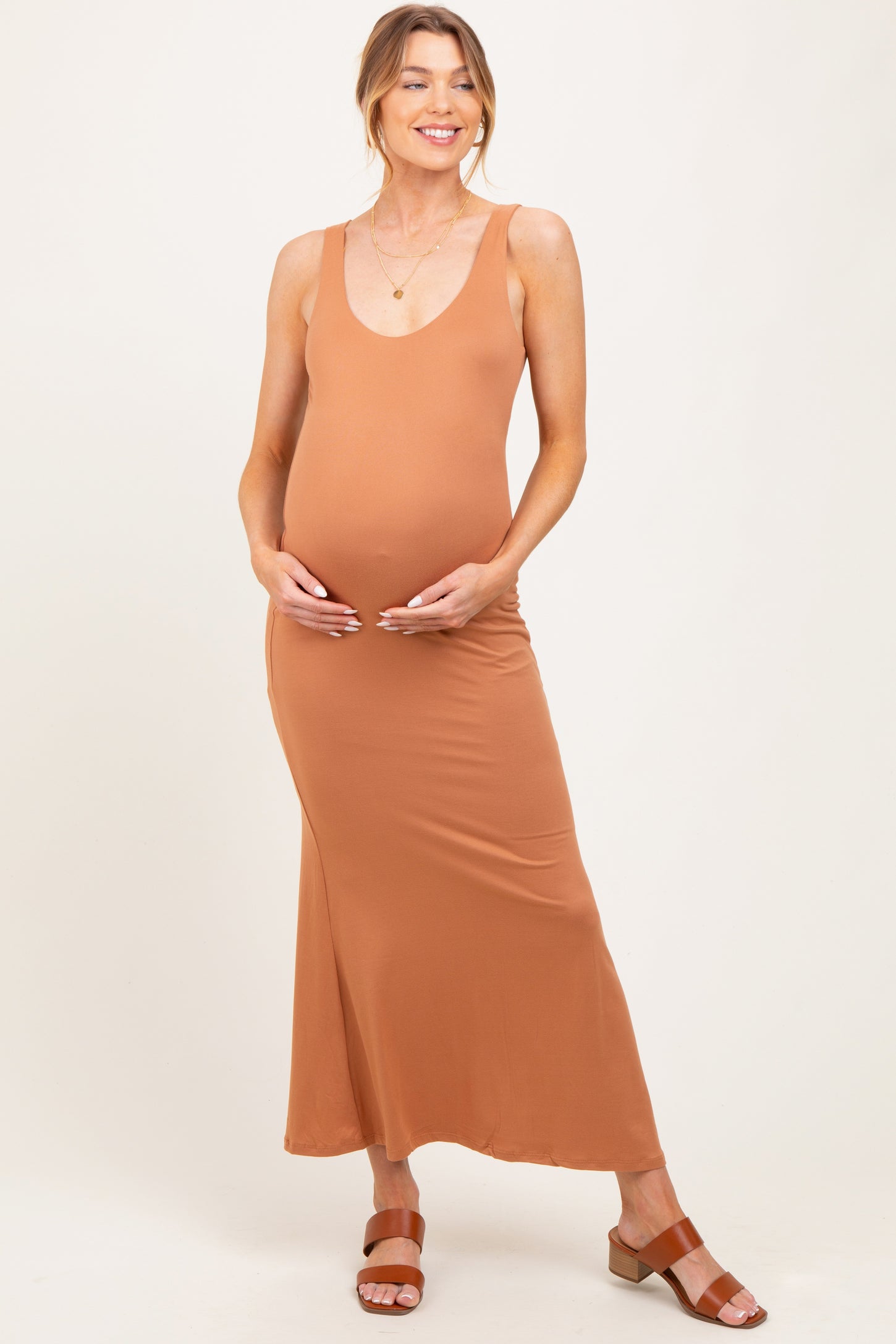 woman wearing a rust-colored maternity maxi dress and holding her baby bump