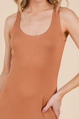 woman wearing a tan sleeveless bodycon dress, showcasing a fitted silhouette and scoop neckline