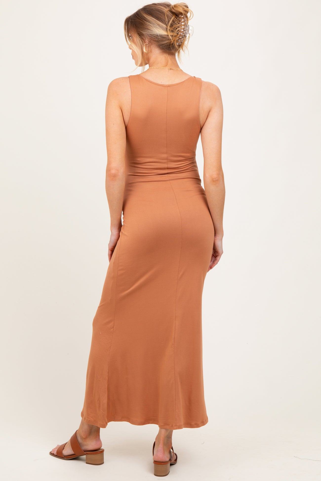 woman wearing a rust-colored sleeveless maternity maxi dress, showing a fitted silhouette and back view