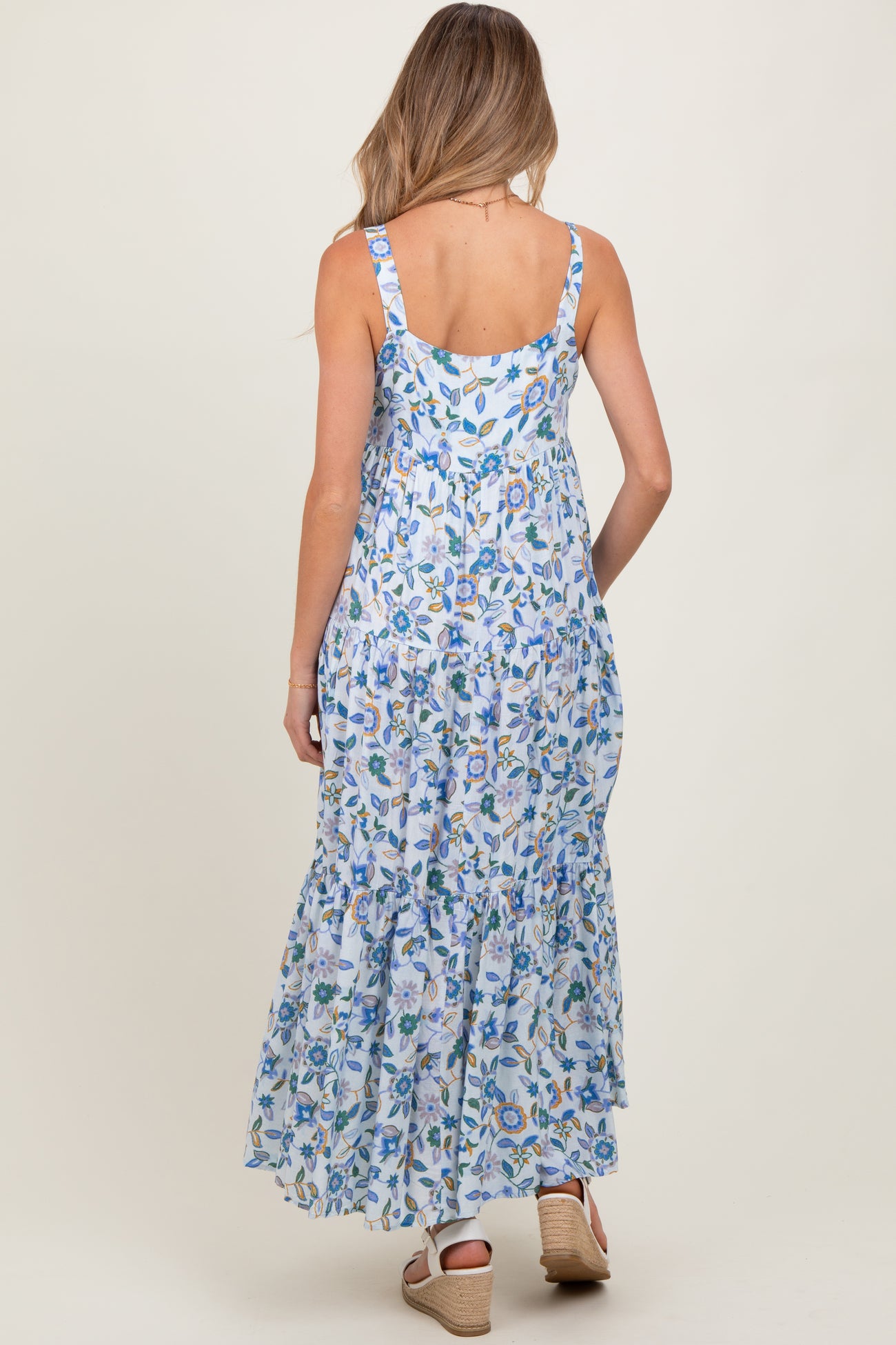 woman wearing a floral blue maternity maxi dress with a tiered ruffle hem, showing her back and straps